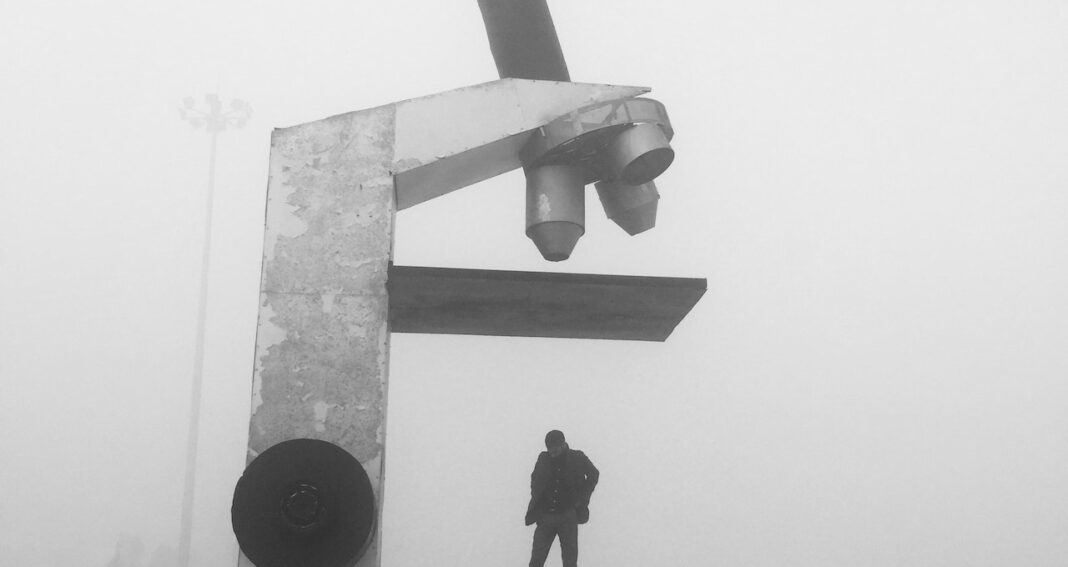 Sculpture of microscope with man on platform underneath in black and white.