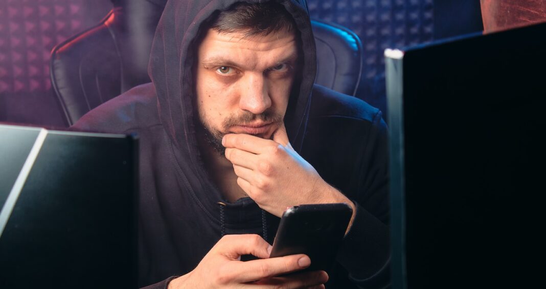 Employees sometimes take cyberloafing breaks at work like this man who is using his phone at his computer workstation.