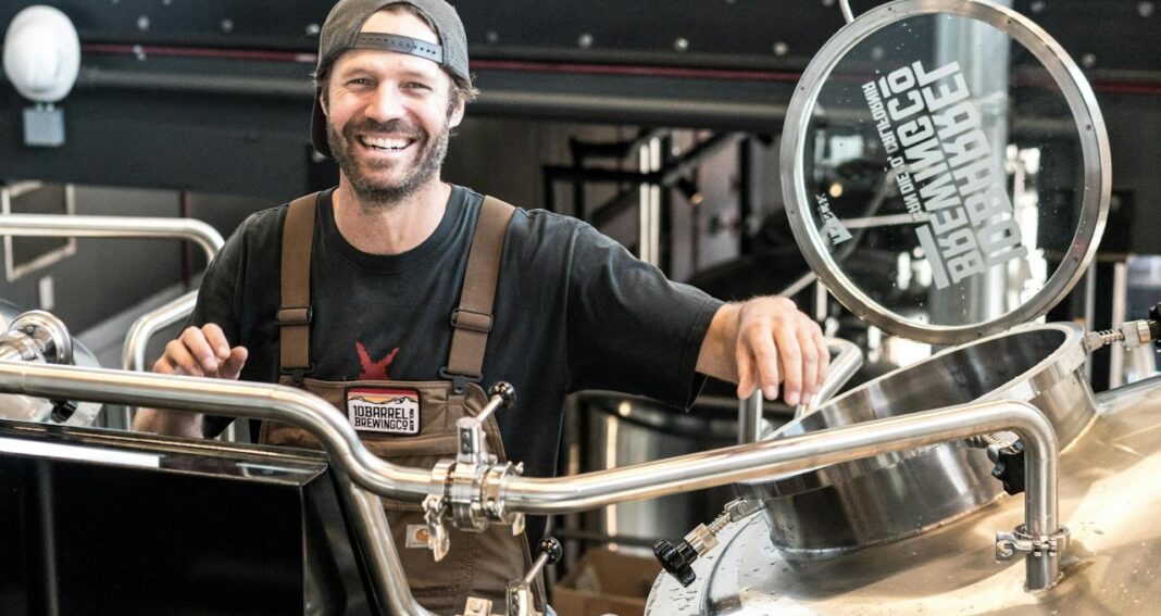 Smiling man in black shirt in front of factory machinery.