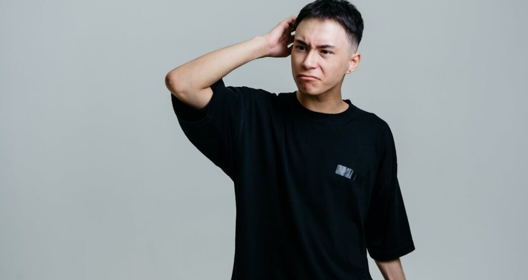 Man in a black t-shirt scratching his head and looking puzzled.